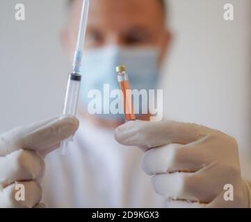 Medico che indossa Guanti di protezione e maschera facciale tenere in mano un'iniezione con un vaccino, antidoto, e il trattamento per Covid-19 Virus Pandemic Foto Stock