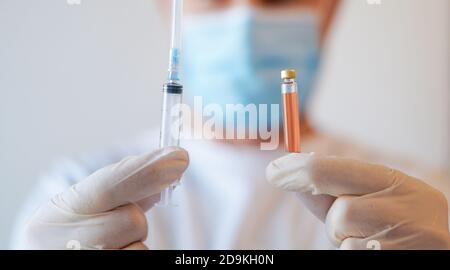 Primo piano di un operatore medico irriconoscibile che indossa una maschera protettiva e. Guanti contenenti siringa con vaccino Covid-19 Foto Stock