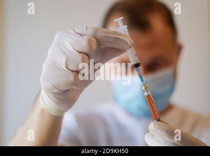 Primo piano di un operatore medico irriconoscibile che indossa una maschera protettiva e. Guanti contenenti siringa con vaccino Covid-19 Foto Stock