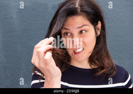 Primo piano ritratto giovane donna che tiene i capelli con espressione infelice Foto Stock