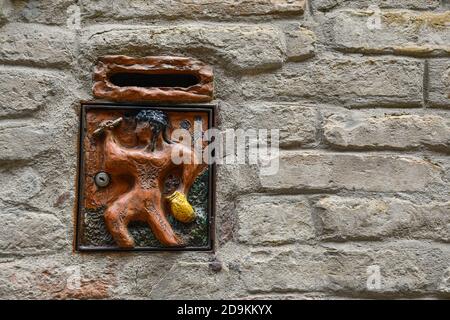 Una moderna cassetta postale decorata con un bassorilievo raffigurante un pugile etrusco, uno sport popolare nell'antica Etruria, su un muro di pietra, Siena, Toscana, Italia Foto Stock