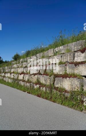 Germania, Baviera, alta Baviera, distretto di Altötting, parete argentata, rinforzo pendenza, blocchi di granito, surcresciuto, accanto ad una strada Foto Stock