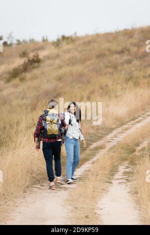 Donna afroamericana sorridente che guarda il ragazzo con lo zaino mentre passeggiata sul sentiero durante il viaggio Foto Stock