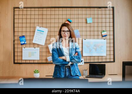 Attraente donna d'affari in occhiali in piedi nell'ufficio moderno. Foto Stock