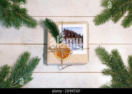 Confezione regalo in stile eco-friendly: Carta naturale ruvida, corda di iuta, ramoscelli di abete rosso su sfondo di legno bianco. Foto Stock