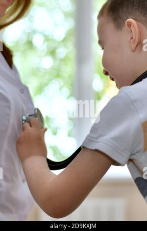 Il bambino sorride e applica uno stetoscopio al accappatoio bianco del medico. Foto Stock