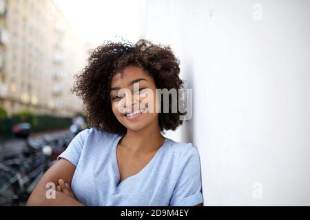 Primo piano ritratto sorridente giovane afroamericana con riccia capelli appoggiati alla parete esterna Foto Stock