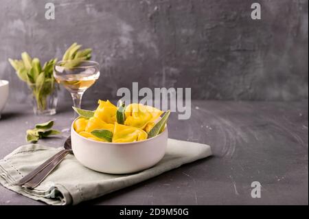 Grandi tortelloni con ricotta e salvia su fondo grigio. Pasta italiana e vino bianco. Cucina tradizionale bolognese, regione Emilia Romagna. Foto di alta qualità. Spazio di copia. Foto Stock