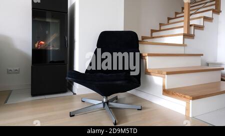 Moderno soggiorno scandinavo con poltrona blu navy, scala e un moderno caminetto indipendente contemporaneo. Foto Stock