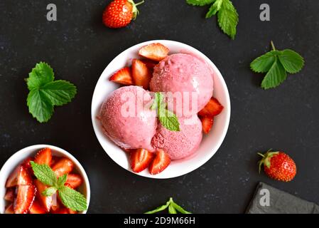 Gelato alla fragola in ciotola su fondo di pietra scuro. Vista dall'alto, disposizione piatta Foto Stock