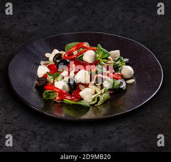 Insalata mista con mozzarella, semi d'oliva e verdure fresche su sfondo scuro Foto Stock