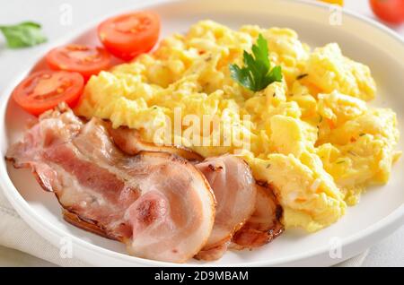 Uova strapazzate, pancetta fritta e pomodori su piatto bianco, vista ravvicinata Foto Stock