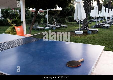 Belek, Turchia - Ottobre 2020: Nessuno gioca a ping pong all'esterno. Hotel sopravvissuti durante la quarantena. Racchetta su un tavolo blu, prato con lettini vuoti Foto Stock