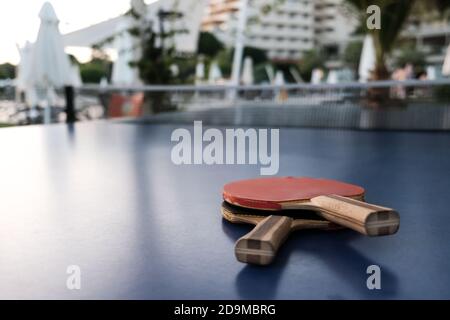 Vista ravvicinata di due racchette da ping pong su superficie blu. Messa a fuoco selettiva, hotel o parco su sfondo sfocato. Divertente concorso per due Foto Stock