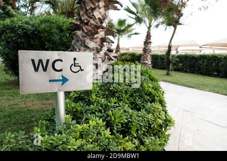 WC segno ad una stanza o toilette o bagno o toilette incluso servizio per invalidi o disabili. Splendidi alberi tropicali verdi e autobus Foto Stock