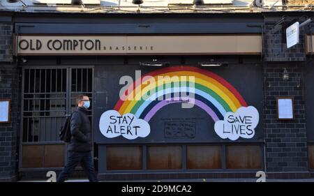 Un uomo con una maschera facciale cammina oltre un cartello Stay Alert, Save Lives Rainbow in un ristorante chiuso in Old Compton Street a Soho, Londra, durante il secondo blocco nazionale in Inghilterra. Foto Stock