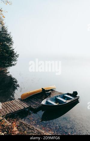 Molo vuoto con barche legate in una mattina foggy su un lago calmo. Foto Stock