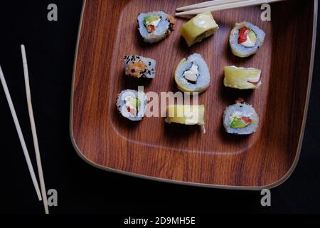 Primo piano di panini di sushi con bastoncini in un piatto di legno Foto Stock