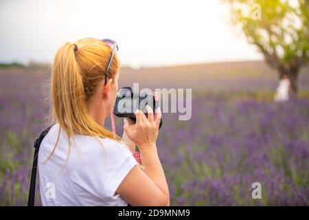 Donna con fotocamera sul campo. Ragazza che scatta foto nel campo dei fiori di lavanda. Paesaggio naturale idilliaco, fotografo di viaggio Foto Stock