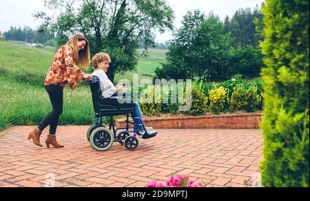 La donna che porta la sua madre in una sedia a rotelle Foto Stock