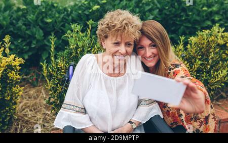 Ragazza che prende selfie con la madre in sedia a rotelle Foto Stock