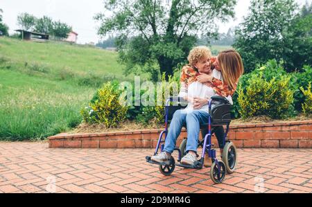 Figlia abbracciando la madre anziana in sedia a rotelle Foto Stock