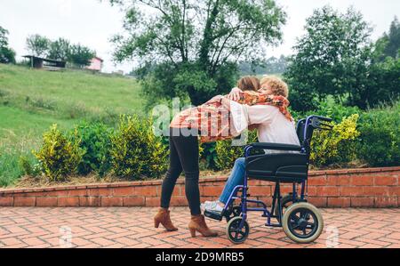Figlia abbracciando la madre anziana in sedia a rotelle Foto Stock