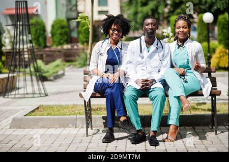 Tre medici del gruppo afroamericano con stetoscopio che indossa cappotto da laboratorio seduto sulla panca. Foto Stock