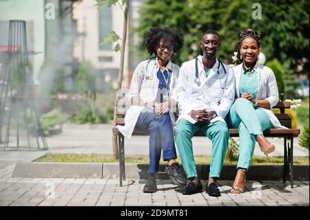 Tre medici del gruppo afroamericano con stetoscopio che indossa cappotto da laboratorio seduto sulla panca. Foto Stock