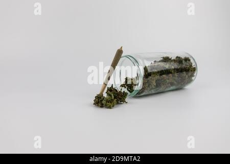 Vaso di vetro pieno di boccioli di marijuana, fiori di marijuana essiccati e una sigaretta di marijuana. Isolato su sfondo bianco. Dolce dipendenza Foto Stock