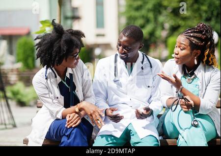 Tre medici del gruppo afroamericano con stetoscopio che indossa cappotto da laboratorio seduto sulla panca. Foto Stock