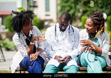 Tre medici del gruppo afroamericano con stetoscopio che indossa cappotto da laboratorio seduto sulla panca. Foto Stock