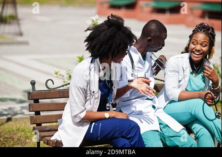 Tre medici del gruppo afroamericano con stetoscopio che indossa cappotto da laboratorio seduto sulla panca. Foto Stock