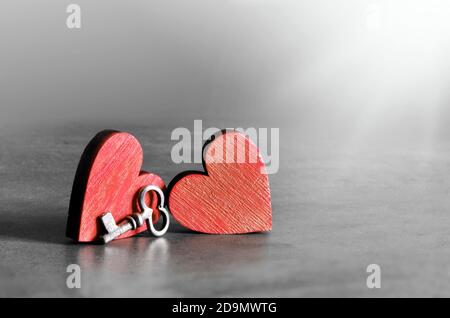 Chiave in argento e cuori in legno rosso su sfondo grigio. San Valentino. Concetto di vacanza. Foto Stock