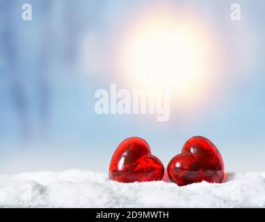 Due cuori di vetro rosso nel parco sulla neve. Concetto di festa invernale. Foto Stock