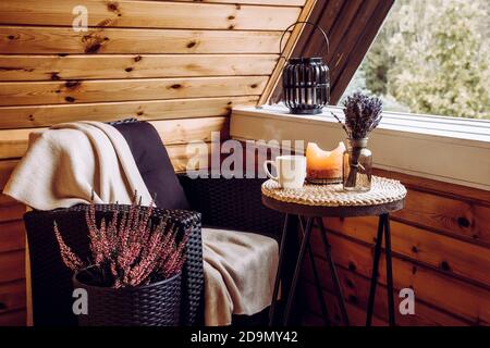 Carino autunno hygge decorazione domestica arrangiamento. Minuscolo balcone con cabina in legno con fiori di erica, lavanda in vaso bottiglia, fiamma a lume di candela, plaid morbido. Foto Stock