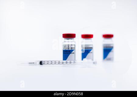 3 flaconcini di vaccino COVID-19 uno accanto all'altro con una siringa su fondo bianco e fuoco selettivo. Concetto di coronavirus Foto Stock