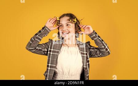 ragazza felice in arricciacapelli che gioca parrucchiere salone. Punte facili che fanno la acconciatura per i bambini. Attrezzi per la cura dei capelli e accessori per i capelli. Capretto con le macchie sul viso. Posa con i arricciacapelli Foto Stock