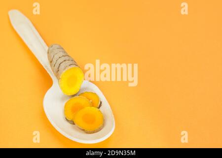 Radici curcuma in un cucchiaio di legno su sfondo arancione Foto Stock