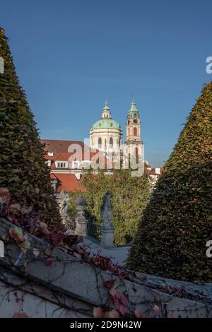 Una vista tra gli alberi attraverso il giardino di Vrtbovska verso la chiesa barocca di San Nicola della città bassa di Praga. Foto Stock
