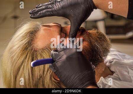 Grande tempo al barbiere. Barbuto al parrucchiere. Barbiere professionale con cliente maschile. Hipster con barba e baffi. Uomo vuole un nuovo acconciatura. Bellezza e moda. Uomo maturo al barbiere. Foto Stock