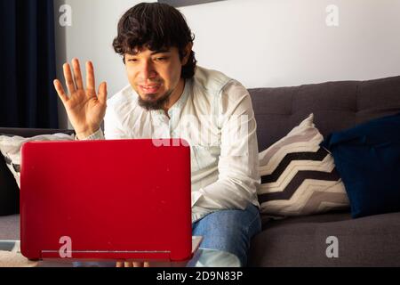 Giovane ispanico che indossa abiti casual durante una videochiamata con un computer portatile molto felice ed espressivo chiuso a casa a causa di quarantena Foto Stock