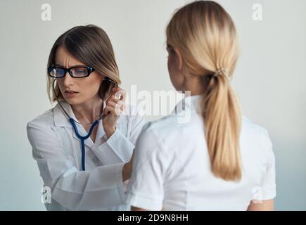 Il medico ascolta il battito cardiaco del paziente attraverso uno stetoscopio su uno sfondo chiaro vista ritagliata Foto Stock