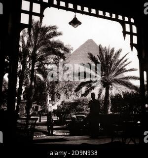 ANNI '40 ANNI '50 LA GRANDE PIRAMIDE DI GIZA DA CASA MENA INGRESSO ACCANTO A DUE UOMINI DI STATO ANONIMI DALLA SILHOUETTE CHE INDOSSANO FEZ CAIRO EGITTO - R15446 RGE001 HARS PERSONE SCENIC MASCHI EGITTO EGIZIANO B&W RESORT TIME OFF SOGNI AVVENTURA GIZA SILHOUETTE VIAGGIO FUGA ECCITAMENTO FAMOSO DURANTE LE FESTE UMORE PASSATO LA CULTURA DI LUSSO FEZ PYRAMIDS ANONYMOUS AURA AMBIENTE OSPITALITÀ PALME PALME PALME PERSONALE VACANZE 1869 NERO E BIANCO VECCHIO STILE Foto Stock