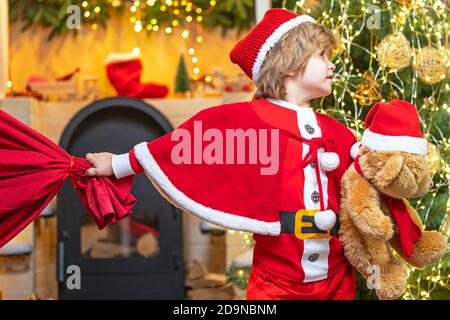 Vacanza in famiglia. Ragazzo bambino giocare vicino albero di natale. Desidera incontrare babbo natale. Aiutante Babbo Natale con borsa grande piena di regali. Credete nel natale Foto Stock