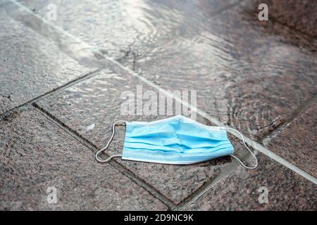 Usato maschera chirurgica contro l'infezione da coronavirus e covid-19 gettato instancabilmente via in un puddle sulla strada, il nuovo immondizia causa env Foto Stock