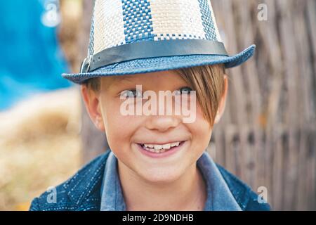 Ragazzo sorridente che gioca con le foglie e guarda la macchina fotografica. Primo piano verticale. Ragazzo carino. Foto Stock