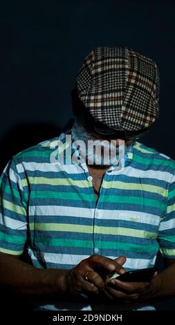 Uomo anziano asiatico con bearded che indossa un cappello e occhiali da sole usando il suo telefono Foto Stock