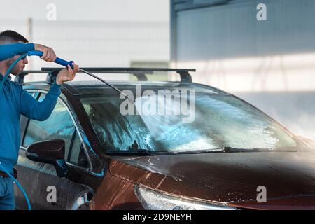Autolavaggio. Uomo pulizia auto con acqua ad alta pressione presso la stazione di lavaggio auto. Foto Stock