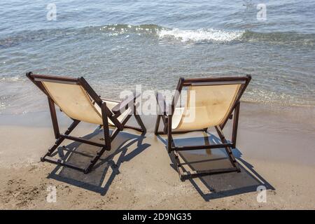 Due sedie a sdraio si trovano sulla spiaggia di sabbia di fronte all' mare Foto Stock